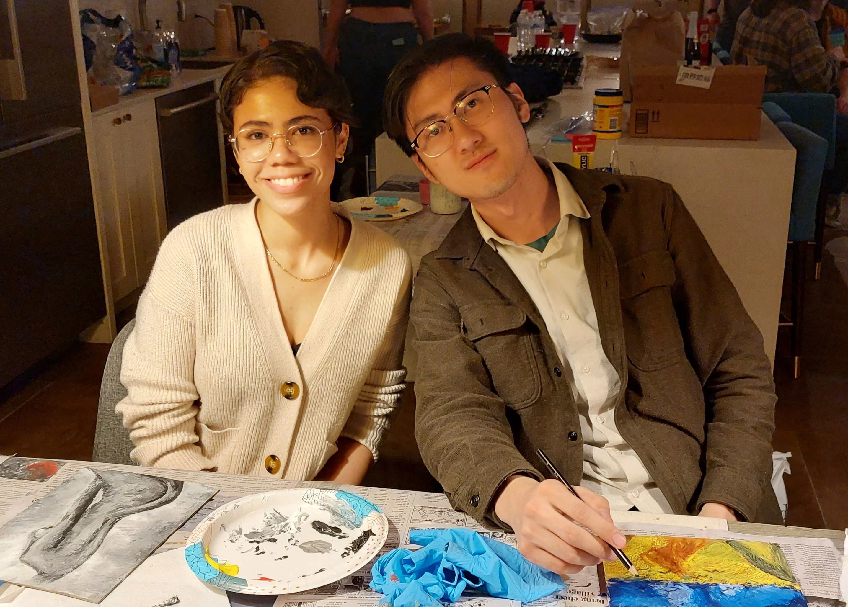 Two participants smiling at the workshop table with paintings in progress